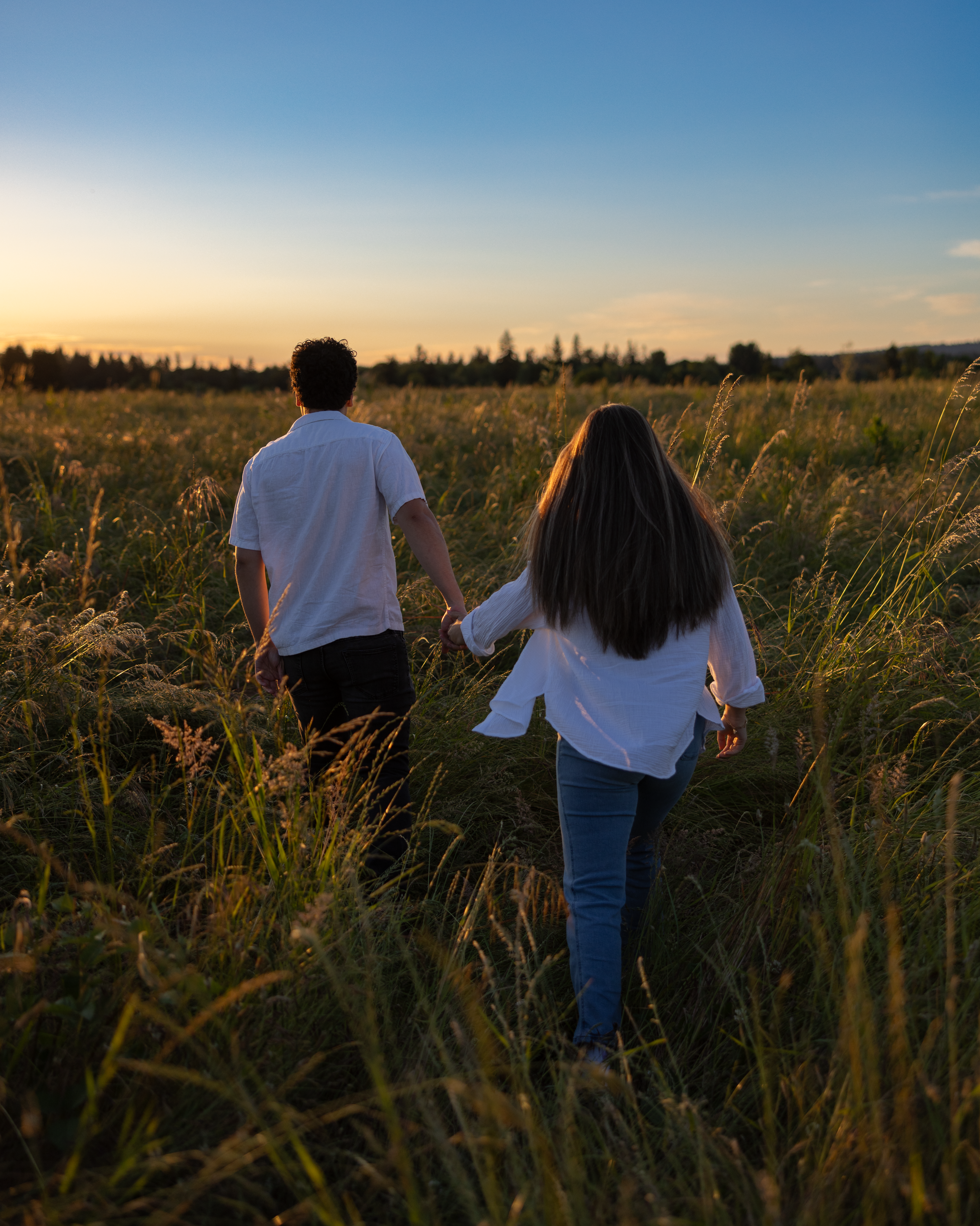 Couple walking hand-in-hand through a golden field at sunset